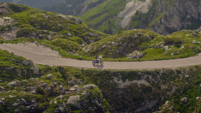 Model riding a XL750 Transalp motorcycle on the road in mountain location.