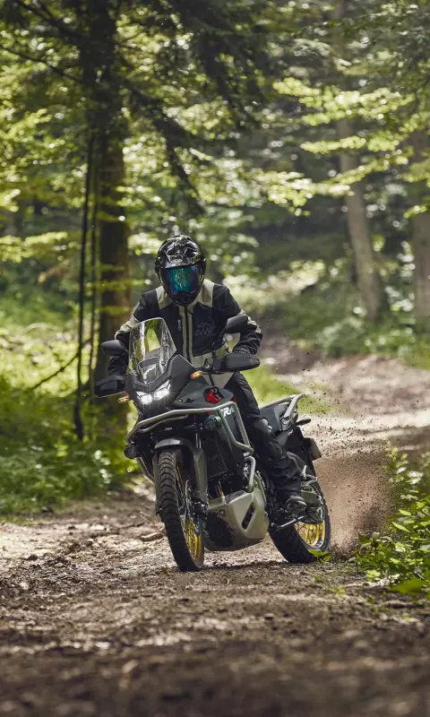Model riding the XL750 Transalp motorcycle in a forest location.